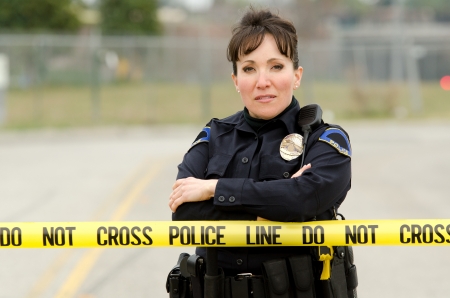 A female police officer standing in behind yellow crime scene tape.の写真素材