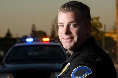 A smiling police officer with his patrol car in the background  の写真素材