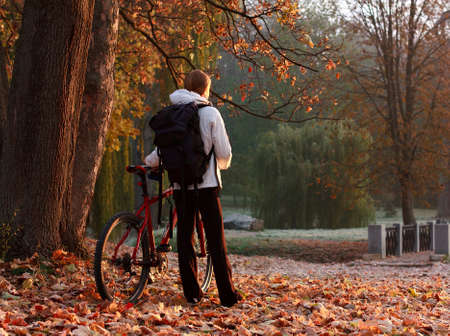 Woman cyclist with bike and backpack in autumn park, lit morning sunの写真素材