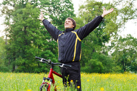 Excited happy man cyclist among the green blooming nature hands outstretched embracing vitality...