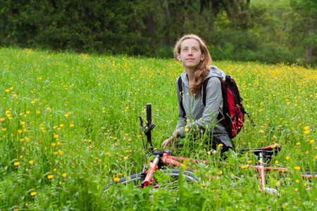 Happy woman cyclist with bike and backpack among of green blooming nature in springの写真素材