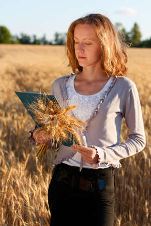 Woman agronomist with document in hand analyzing wheat ears against a background of wheat fieldの写真素材