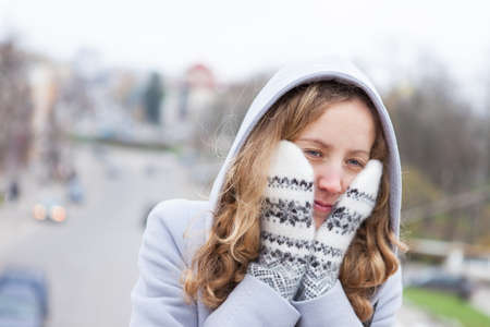 Frozen young woman heated by wool mittens and a from hood against the blurred background city  Outdoorの写真素材