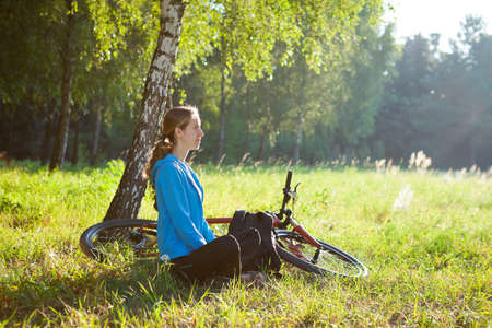 Woman cyclist enjoying relaxation in sunny park sitting in the fresh green grassの写真素材