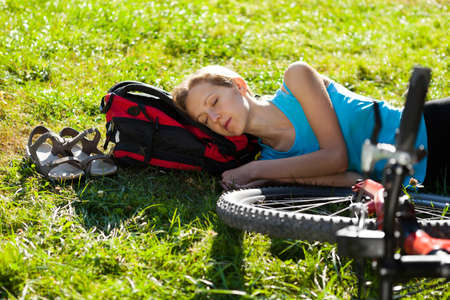 Young girl cyclist enjoying sleeps relax lying in the fresh grass on spring sunny meadow. Outdoorの写真素材
