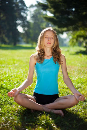 Young girl in lotus pose in the summer park. Yoga outdoorsの写真素材