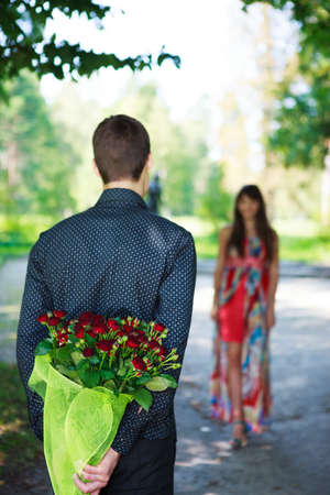 Romantic young man giving a bouquet of red roses to his girlfriend. Sunny parkの写真素材
