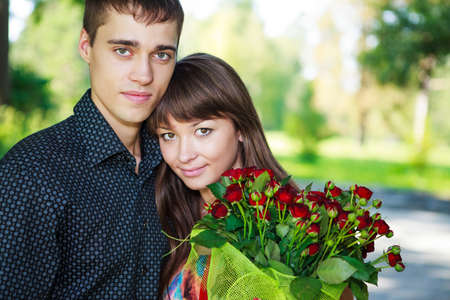 Portrait beautiful lovers young couple with a bouquet of red roses. Sunny summer outdoorの写真素材