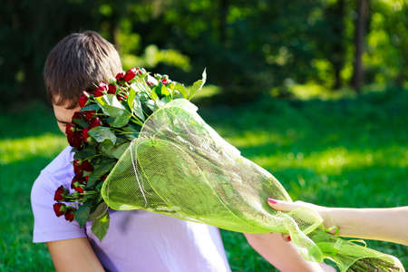 Young man gets hit in the face bouquet of red roses  The sunny nature of the backgroundの写真素材