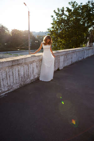 Beautiful girl in a white dress in the rays and glare of the sun in the city in the morningの写真素材