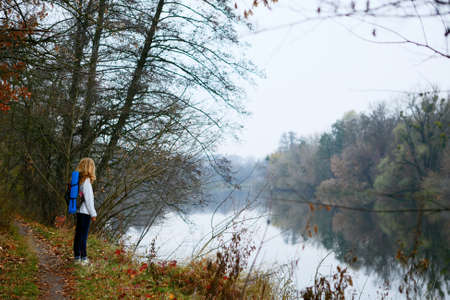 Woman traveler on the coast of forest river. Tourist walking in the weekend. Autumn