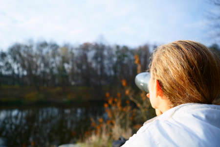 Woman hiker drinking tea from a thermos on the autumn nature. Active Lifestyleの写真素材