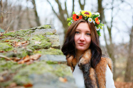 Autumn woman portrait with flowers wreath in fur coat near a stone wall. Autumn seasonの写真素材