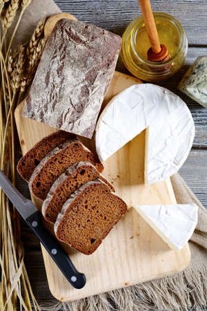 Black bread, brie cheese, knife and honey on a cutting board. Top view