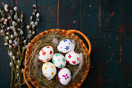 Painted Easter eggs in basket and willow branches on wooden table. Spring holiday