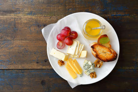 Cheese plate with honey, grapes, bread and walnuts on old wooden board. Top viewの写真素材