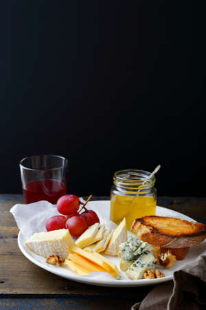 Cheese plate with grapes, honey, bread, walnuts and wine on black background. Delicatessenの写真素材