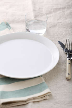 Dinner empty plate, fork, knife and glass water on the striped napkin. Dishwareの写真素材