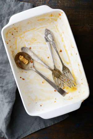 Dirty baking dish with used fork and spoon on wooden background. Top viewの写真素材