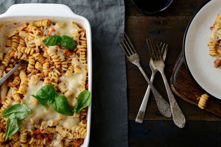 Pasta Bolognese, cheese and basil in baking dish and on plate, three forks on a old wooden table. Top viewの写真素材