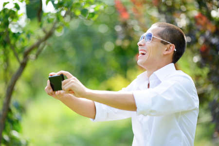 Laughing young man in sunglasses taking selfie in summer outdoors