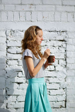Pretty young woman with a morning disposable coffee cup on the background old brick wallの写真素材