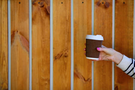Coffee to go. Disposable cup in woman hand on background of wooden planksの写真素材