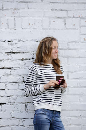 Smiling girl with a disposable coffee cup on the background old brick wallの写真素材