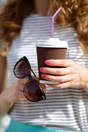 Disposable Coffee Cup and Sunglasses in the hands of woman. Closeupの写真素材