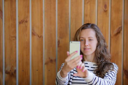 Young smiling woman taking selfie on the background of wooden wall