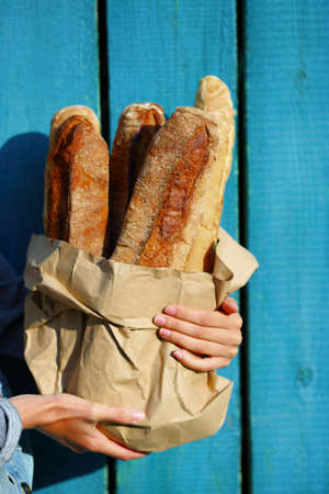 Baguettes. Paper bag with baguette in hands of woman closeup against the wooden fenceの写真素材