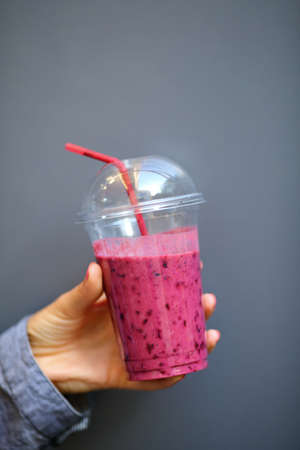 Berry Smoothies. Disposable cup in woman hand closeup against the gray backgroundの写真素材