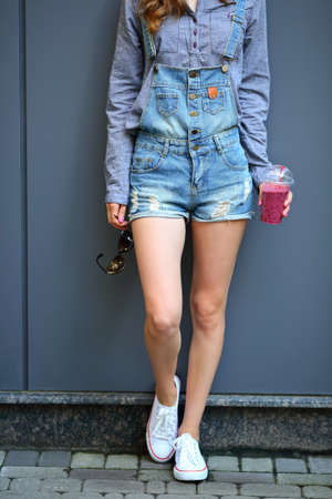 Young woman with a smoothie in disposable cup and sunglasses in their hand on a street. Healthy...