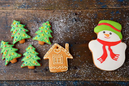 Christmas cookies in the shape of snowman, new year tree and house on old wooden backgroundの写真素材