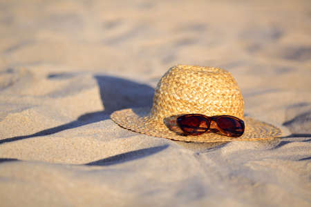 Straw hat and sunglasses illuminated sun on the sand at the beach. Summer vacations conceptの写真素材