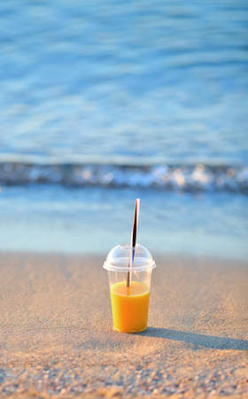 Orange juice in a disposable cup in the sand on the beach. Summer vacations conceptの写真素材