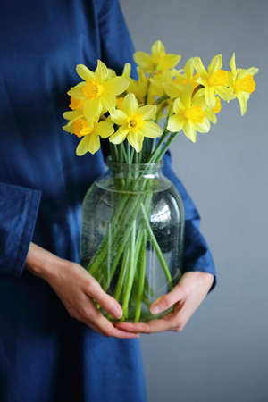 Blooming daffodil in glass jar in woman hands. Sring flowersの写真素材