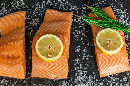 Top view of fresh raw salmon fish steak with spices on a dark stone background. Salt, spices,...