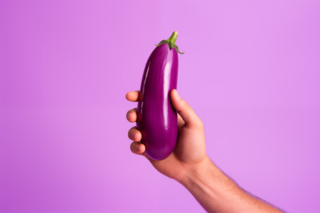 A woman's hand holds an eggplant isolated on a pink background.の素材