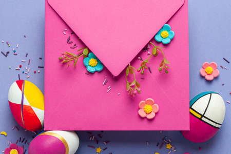 Easter greeting card with cute handmade colorful eggs, kraft pink envelope and flowers on lilac background. Flat lay concept, top view with copy space.の写真素材