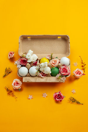 Easter holiday concept with cute handmade colorful eggs, egg tray, bunny and flowers on yellow background. Flat lay concept, top view. An Easter card with a copy of the place for the text.の写真素材