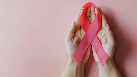 Hands holding pink ribbon on pink background. Concept of breast cancer awareness and women's health.の素材
