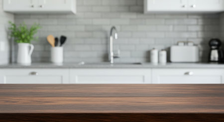 Dark wood table top with blurred kitchen interior in background. Counter with sink, kitchenware, and appliances. Culinary and domestic concept.の素材