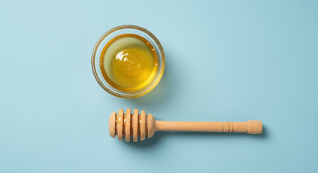 Overhead shot of honey in glass bowl with dipper on blue surface. Sweetener, natural product and healthy eating concept. Copy space.の素材