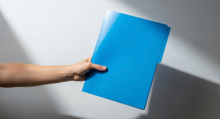 A human hand extends, holding a vibrant blue folder against a plain background with subtle shadows. Represents business, organization, and document management.の素材