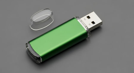 A close up top down professional photo of a metallic green USB flash drive with its clear plastic cap removed, resting on a neutral grey surface. This portable data storage device is ready for use.の素材