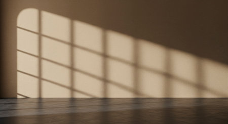 Empty minimalist room with a warm beige wall and dark concrete floor, featuring dramatic arched window shadows cast by natural sunlight.の素材