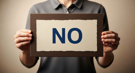 An individual holds up a brown framed sign with the word NO written in blue letters on a textured paper, symbolizing refusal or denial.の素材