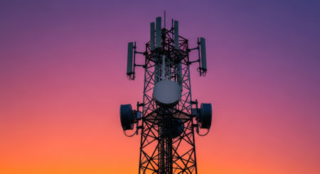 A tall telecommunications tower with multiple antennas and dishes silhouetted against a vibrant sunset sky, showcasing modern communication infrastructure and wireless connectivity.の素材