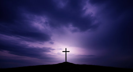 A stark black silhouette of a christian cross stands on a solitary hill against a dramatic dark purple sky with a bright light source.の素材
